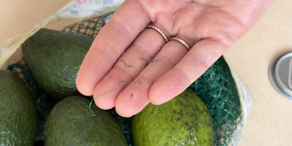 A hand holds green microplastics shed from opening netted avocados.